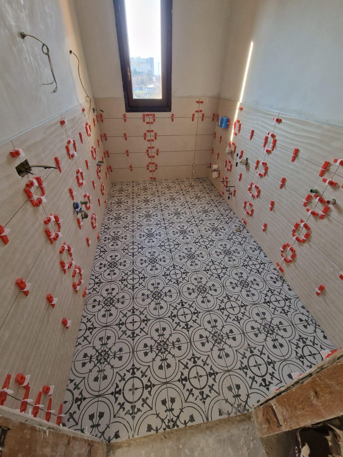 Bagno in ristrutturazione: pareti piastrellate con livellatori rossi e pavimento in cementine bianche e nere a motivo geometrico.