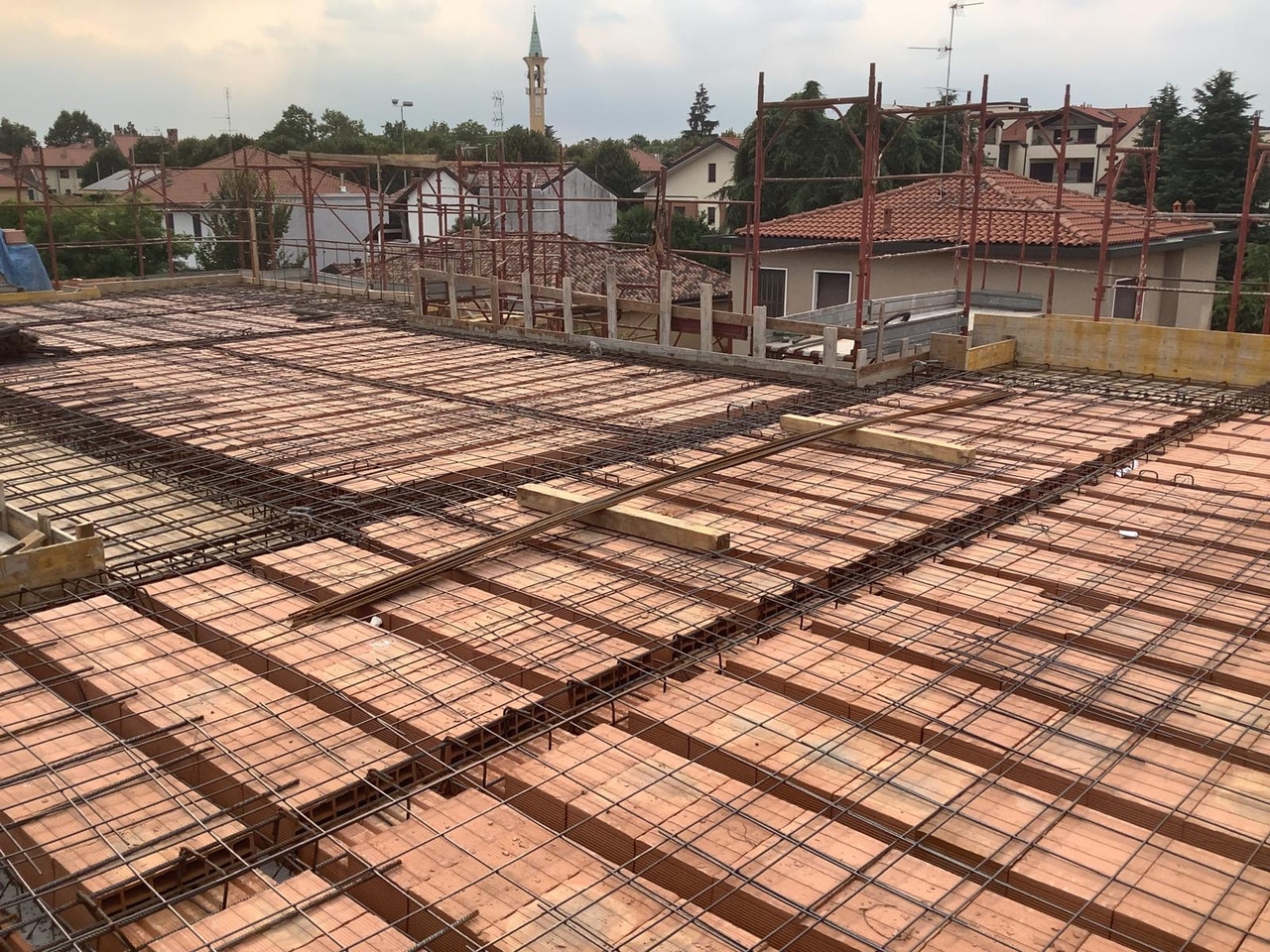 Solaio in laterocemento con armatura in ferro e rete elettrosaldata pronto per il getto, ponteggi e abitazioni sullo sfondo.