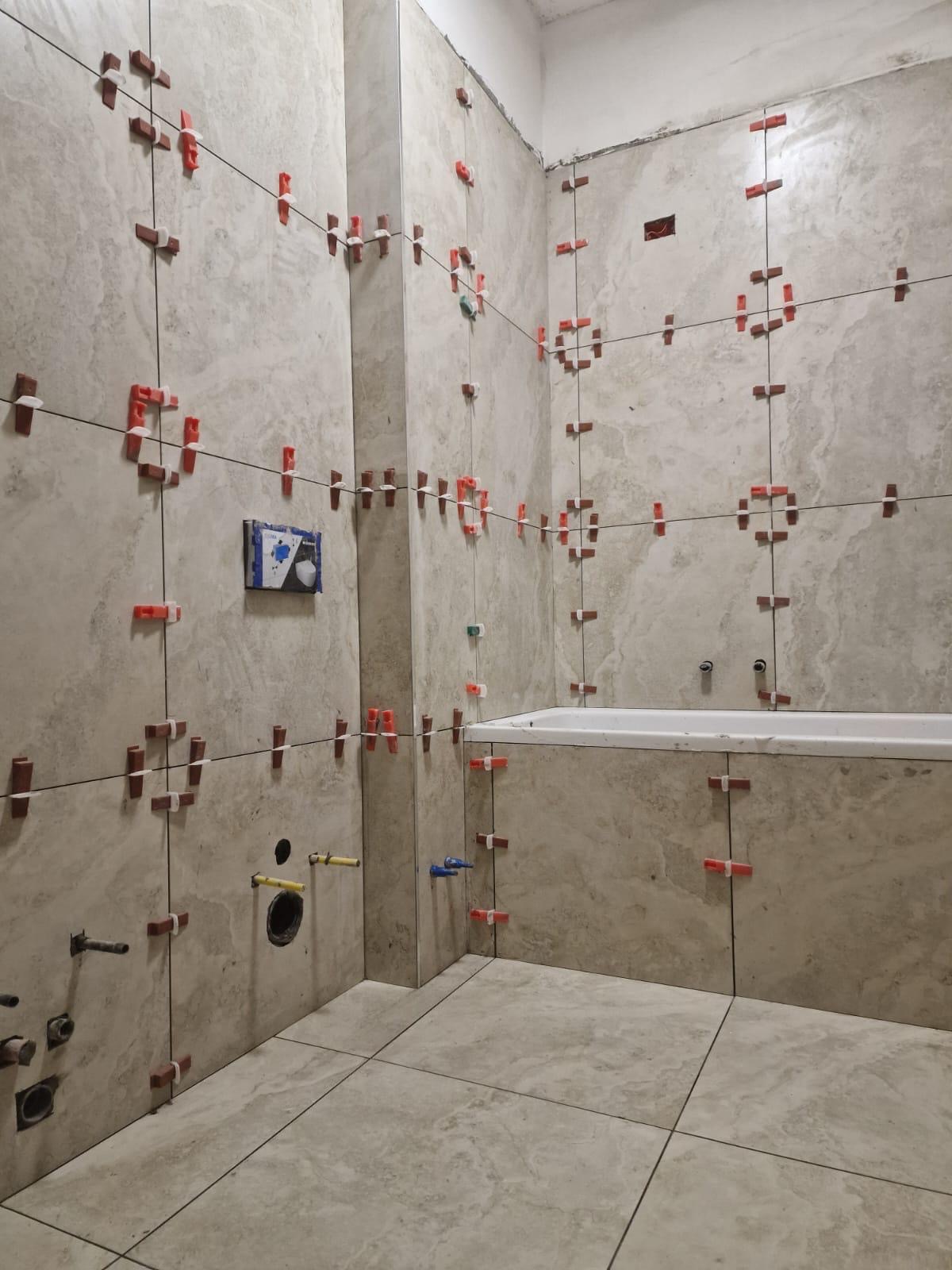 Bagno in ristrutturazione con vasca incassata: pareti e pavimento in gres effetto marmo grigio, posa con livellatori.