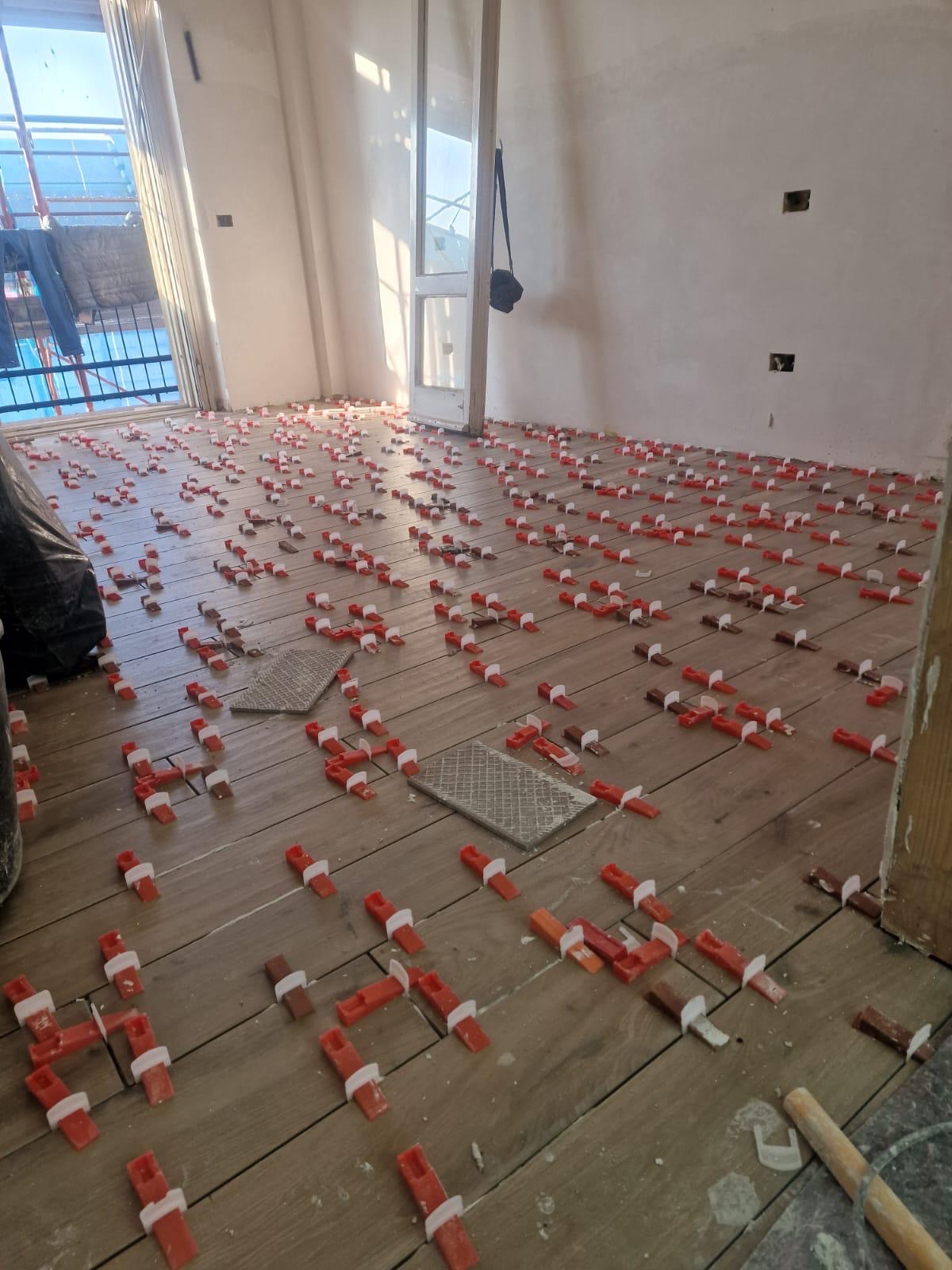 Stanza al grezzo con pavimento in gres effetto legno appena posato, livellatori sui giunti e portafinestra verso il balcone.