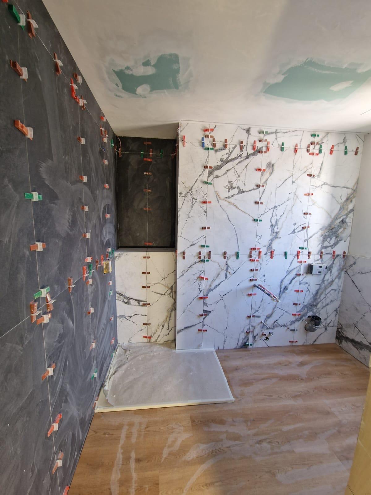 Bagno rivestito con grandi lastre di gres effetto marmo bianco e antracite, con zona doccia e pavimento effetto legno.