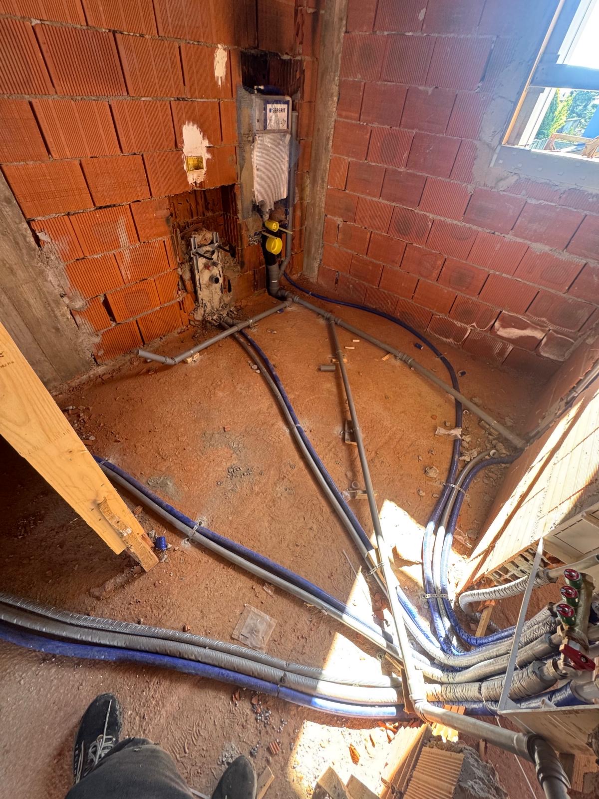 Locale al grezzo in laterizio con cassetta di scarico a incasso e tubazioni idrauliche ed elettriche in posa sul sottofondo.